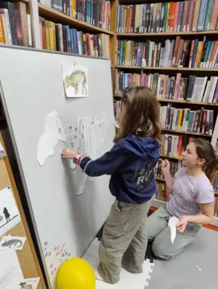 Dwie dziewczynki stoją przy tablicy i układają szkielet dinozaura.