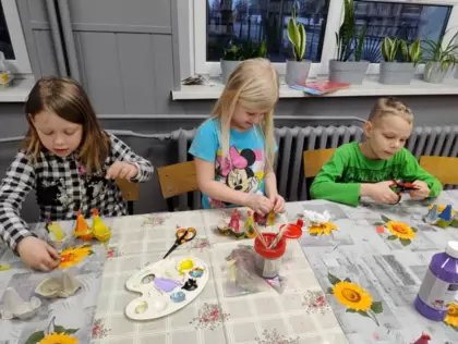 Dzieci siedzą przy stole i wycinają kurki z papieru.