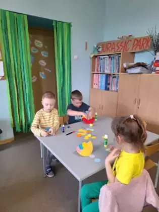 Przedszkolaki przy stoliku wykonują pracę plastyczną.