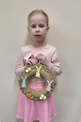 Dziewczynka trzymająca w ręce zrobiony na szydełku wianek wielkanocny.