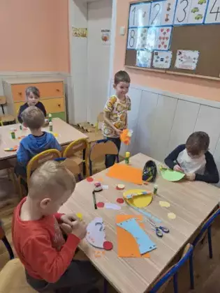 Przedszkolaki przy stoliku wykonują pracę plastyczną.