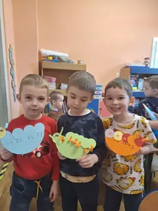 Dzieci trzymają w ręce prace plastyczne przedstawiające stonogę.