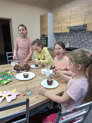 Dziewczyny dekorują lukrem i kolorową posypką babeczki.