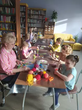 Dzieci słuchają czytanej bajki i owijają włóczką wielkanocne jajko.