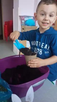 Chłopczyk napełnia doniczkę ziemią