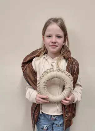 Dziewczynka trzymająca w ręce zrobiony na szydełku wianek wielkanocny.