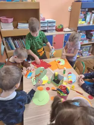 Przedszkolaki przy stoliku wykonują pracę plastyczną.