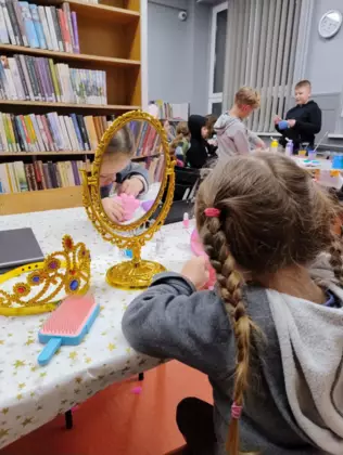 Dziewczynka spogląda do lustereczka w tle dzieci wykonują prace plastyczną.