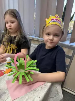 Dziewczynka trzyma w ręce bukiecik kwiatków z papieru.