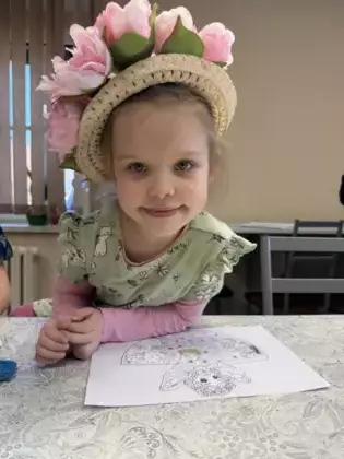Dziewczynka z kapeluszem na głowie koloruje panią wiosnę.