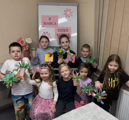 Wspólne zdjęcie po zajęciach dzieci trzymają w rękach bukieciki kwiatków.