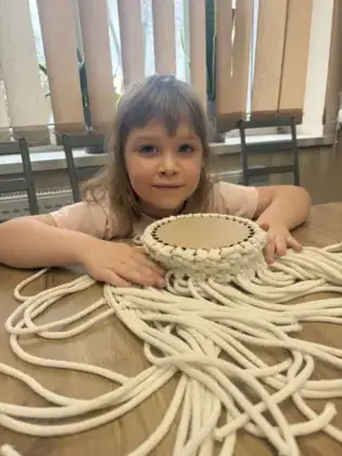 Dziewczyna splata sznurki makramy tworząc koszyczek.