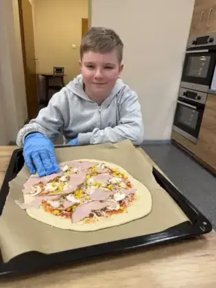 Chłopiec z przygotowaną pizzą gotową do pieczenia.