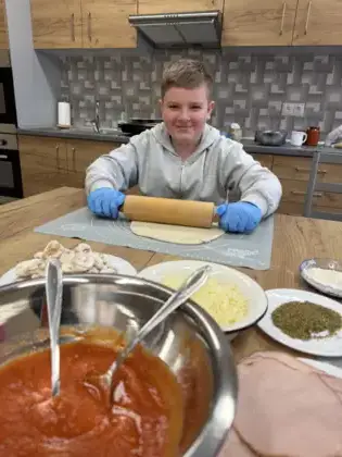 Chłopiec wałkuje ciasto na pizze.