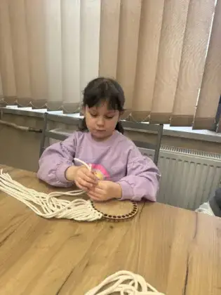 Dziewczynka splata sznurki makramy.