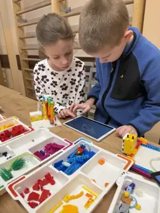 Dziewczynka i chłopiec na tablecie budują z klocków lego.