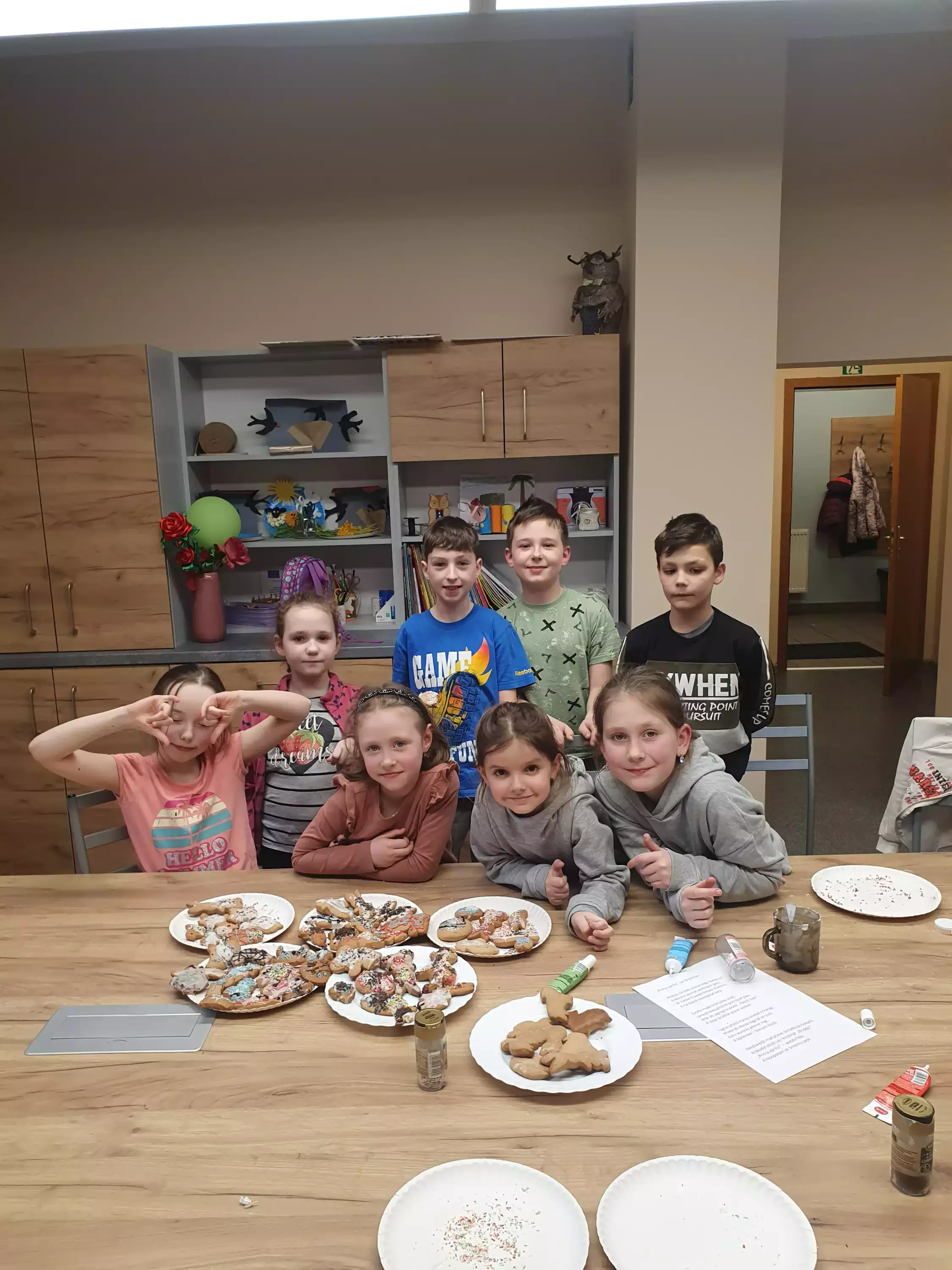 Dzieci stoją wokół stołu na którym leżą upieczone ciasteczka.