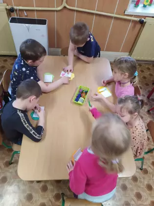 Przedszkolaki siedzą przy stoliku i malują obrazki.