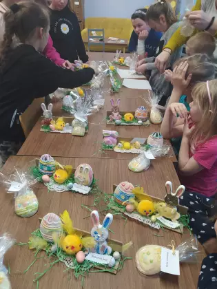 Dzieci stoją przy stole, na którym są ozdoby wielkanocne.