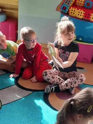 Przedszkolaki siedzą na dywanie i oglądają książki dla dzieci.