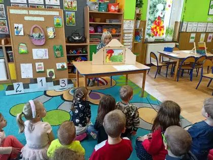 Dzieci siedzą na dywanie i słuchają opowiadania czytanego jako teatrzyk kamishibai.