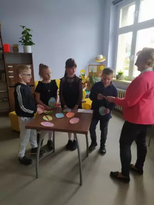 Dzieci stoją przy stoliku i słuchają ogłaszanego wyniku konkursu.