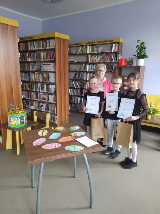 Dzieci stoją w bibliotece w rękach trzymają dyplomy.