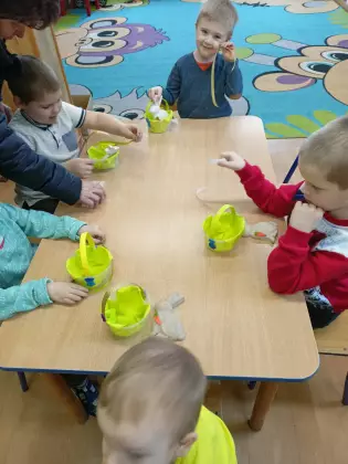 Dzieci przy stoliku wykonują koszyczek wielkanocny.