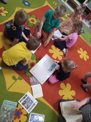 Dzieci siedzą na dywanie i oglądają książeczki.