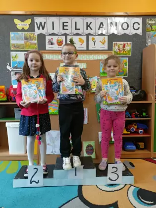 Przedszkolaki stoją na podium trzymając w rękach nagrody konkursowe.