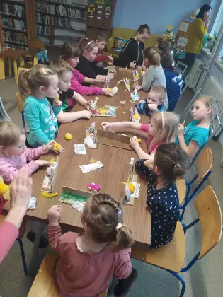 Dzieci siedzą przy stole i wspólnie tworzą ozdoby wielkanocne.