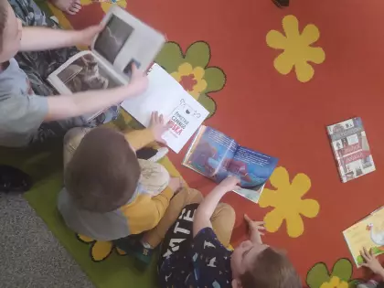 Dzieci siedzą na dywanie w przedszkolu i oglądają książki.
