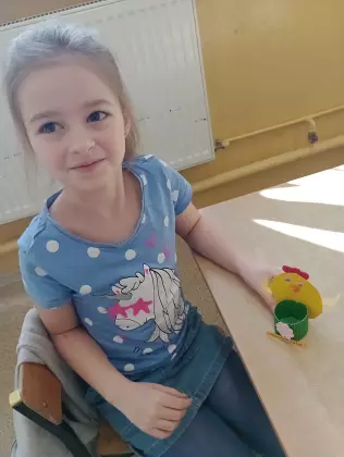 Dziewczynka siedzi na krzesełku i trzyma zajączka w ręce. 