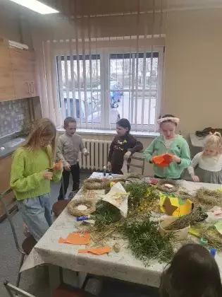 Dzieci przy wspólnym stole wycinają ozdoby na wianek.