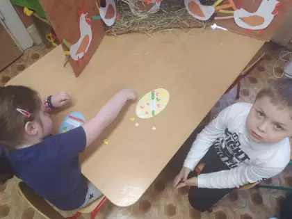 Chłopczyk i dziewczynka siedzą przy stoliku i wykonują ozdoby wielkanocne.