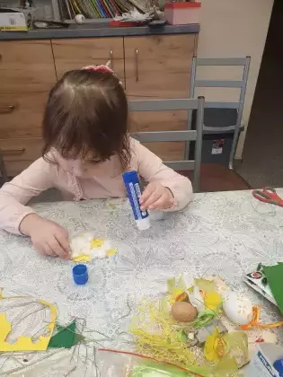 Dziewczynka siedzi przy stole i wykleja baranka.