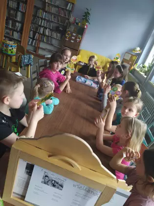 Dzieci siedzą przy stole i słuchają opowiadania czytanego w formie teatrzyku.