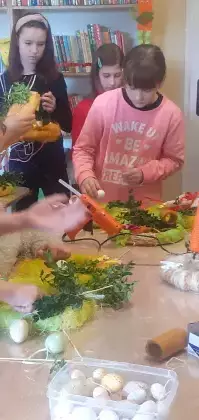 Dzieci przyklejają ozdoby wielkanocne do wianka.