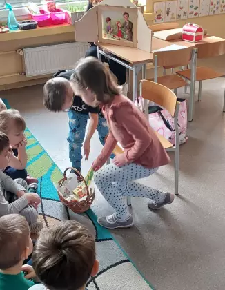 Dzieci wkładają do koszyka wielkanocnego pokarm wycięty z papieru.
