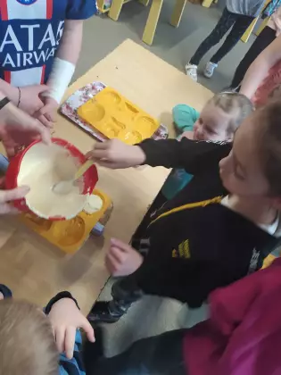 Dzieci stoją przy stole i roztopioną czekoladą wypełniają silikonową formę.