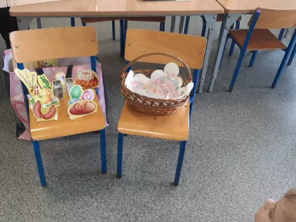 Na krzesełku w przedszkolu stoi koszyczek i wycięty z papieru pokarm wielkanocny.