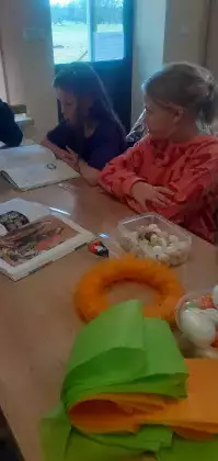 Dzieci siedzą przy stole i czytają książkę.