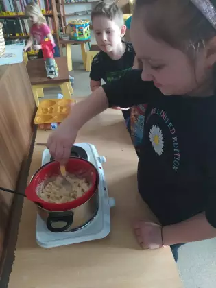 Dzieci na zajęciach roztapiają czekoladę w garnku.