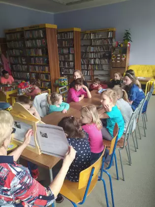 Dzieci słuchają opowiadania czytanego w formie teatrzyku kamishibai.