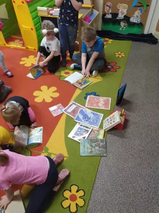 Przedszkolaki siedzą na dywanie i oglądają książeczki.