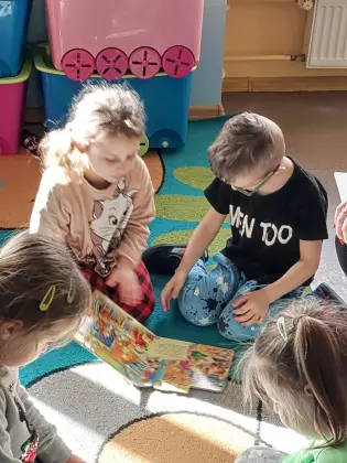Przedszkolaki siedzą na dywanie i oglądają książki dla dzieci.