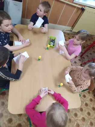 Dzieci siedzą przy stoliku i wykonują pracę plastyczną.