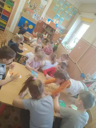 Przedszkolaki siedzą przy stolikach i wykonują prace plastyczne.