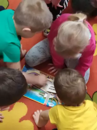 Przedszkolaki na dywanie oglądają książki.
