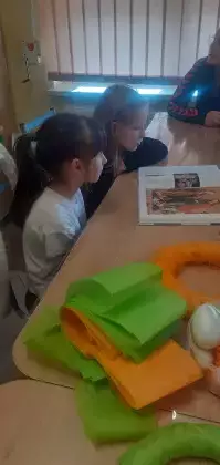 Dzieci siedzą przy stole i czytają książkę.